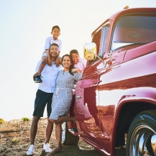 A family of four leaned against a red truck in the field